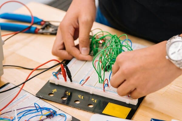 Hands building electronic circuit on breadboard with colorful jumper wires, electronics prototyping and STEM learning
